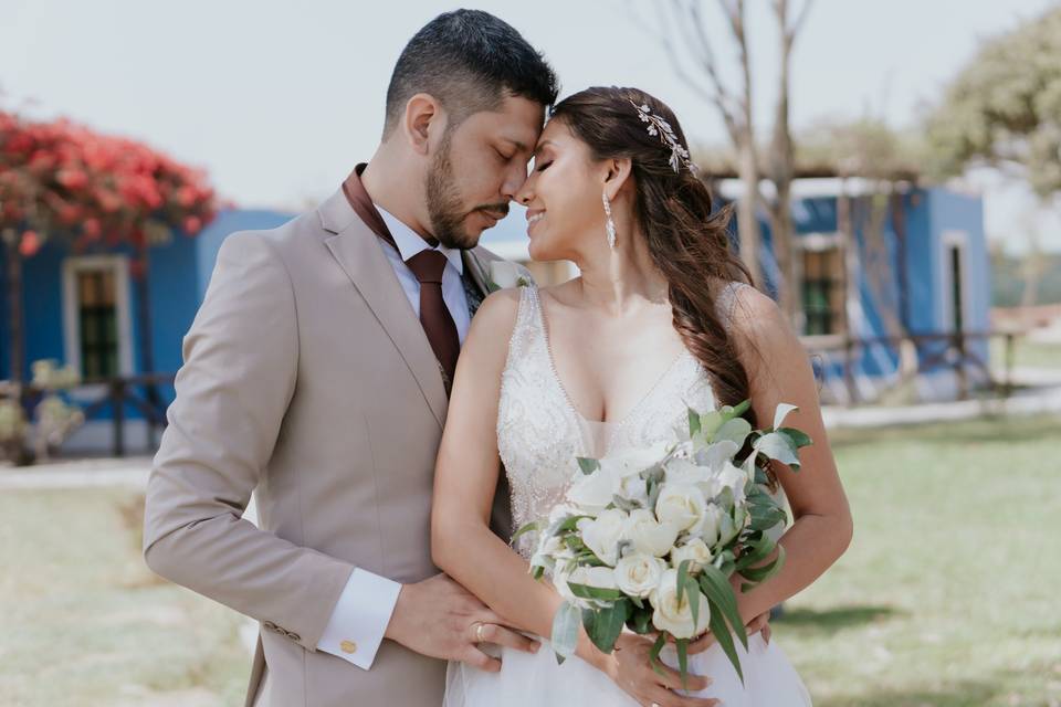 pareja de novio y novia a punto de besarse donde el novio toma de la cintura a su novia mientras ella porta su bouquet