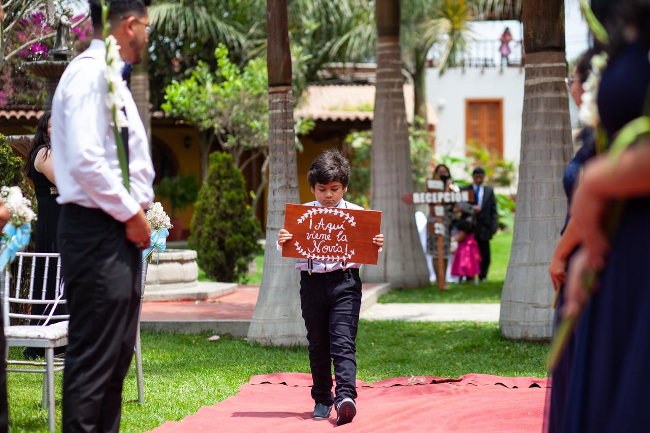 niño caminando camino al altar llevando un letrero que dice aquí viene la novia