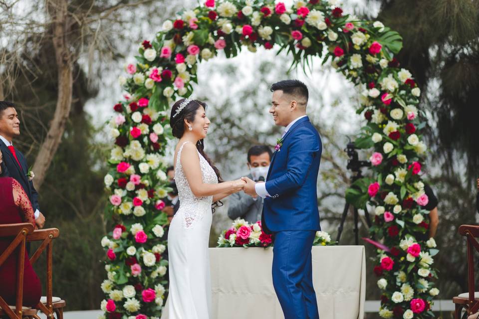 pareja tomada de las manos delante del altar en forma de arco con flores durante su matrimonio