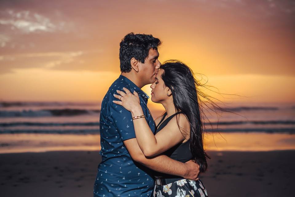 pareja abrazada en la playa con el atardecer de fondo en colores naranjas