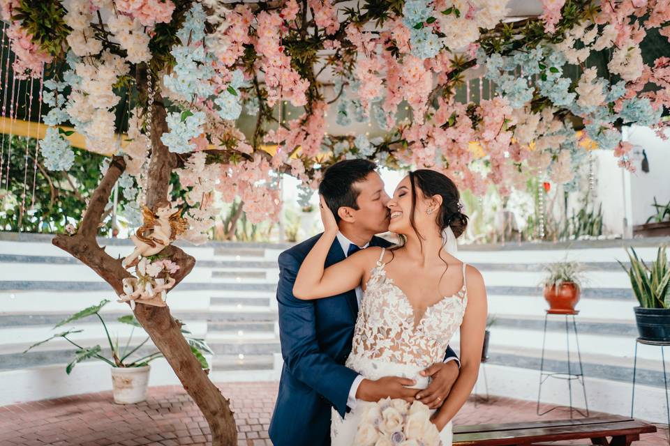 chico y chica besandose delante de decoracion de local para matrimonio con flores rosadas 