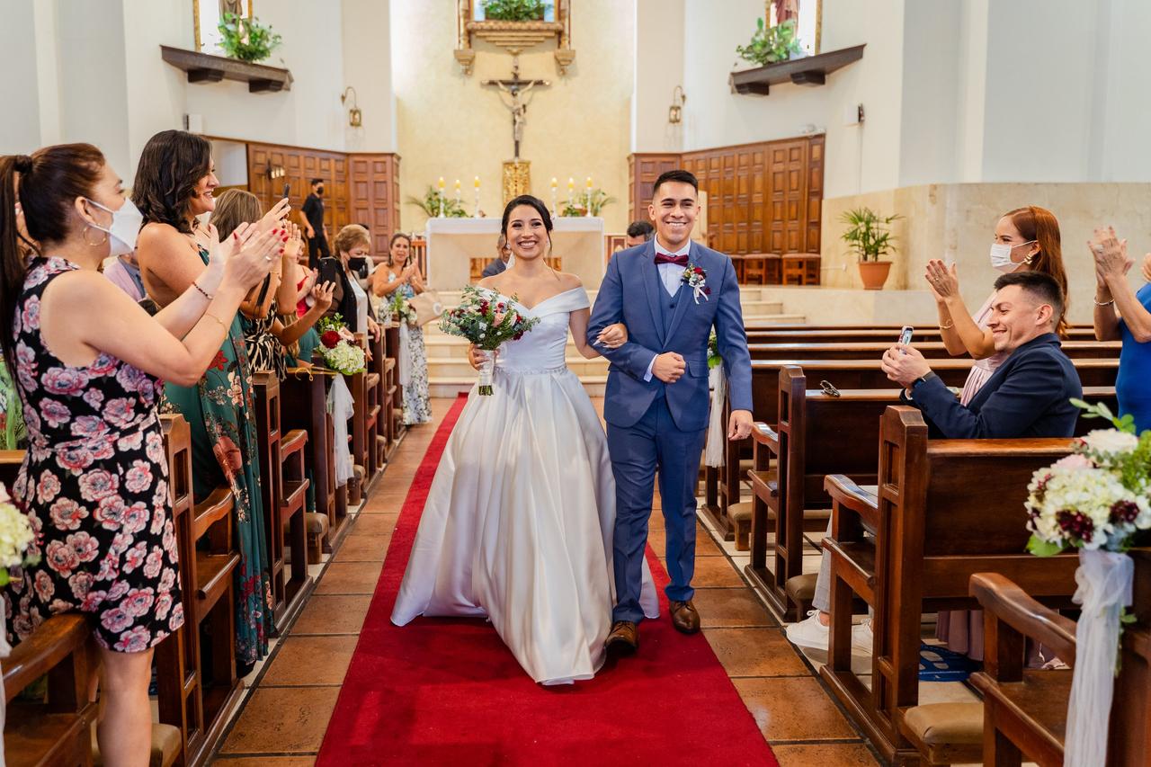 chico con terno caminando del brazo junto a chica vestida de novia en medio de la decoración de iglesia para boda