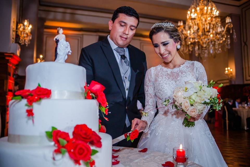 pareja en el corte de la torta de matrimonio blanca con flores rojas y muñequitos de los novios