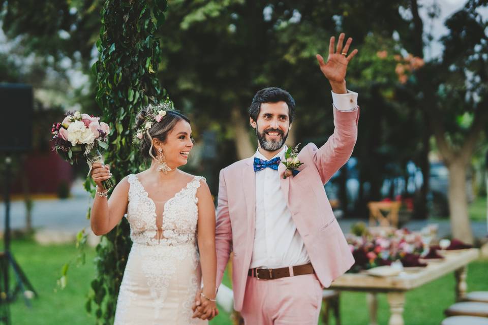pareja de novios tomados de la mano mientras entran a su recepción de matrimonio con el novio con la mano izquierda levantada