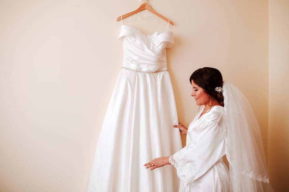 Novia delante de su vestido de novia colgado en la pared antes de vestirlo en su matrimonio
