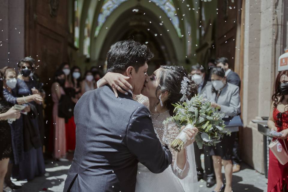 pareja de novios besándose en la salida de la iglesia junto a los invitados con mascarillas lanzándoles arroz