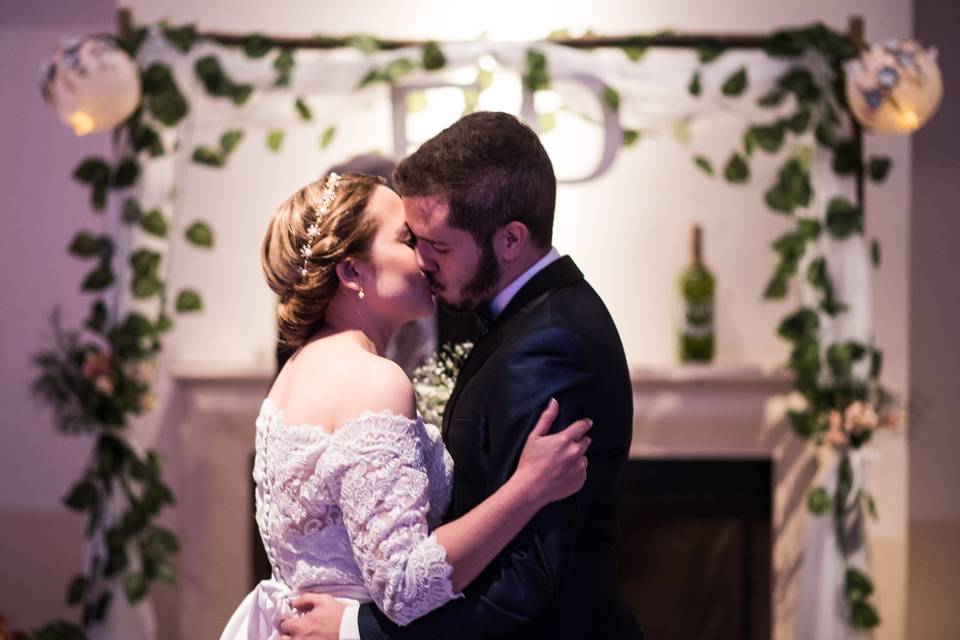 chica vestida de novia besando a chico con terno delante de un arco decorado con follaje