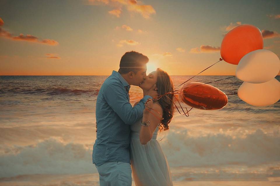 chico y chica besandose frente al mar mientras la chica sostiene globos de colores