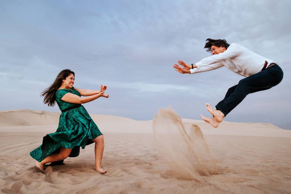 pareja de novios en foto divertida donde la novia mueve las manos como goku y su novio salta como cayendo sobre la arena