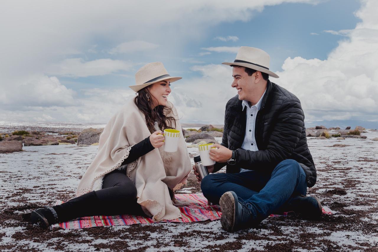 pareja con sombreros y tazas en las manos haciendo un picnic al aire libre