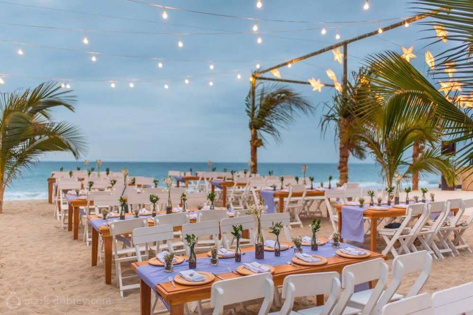mesas de madera con sillas blancas decoradas para una boda en la playa frente al mar