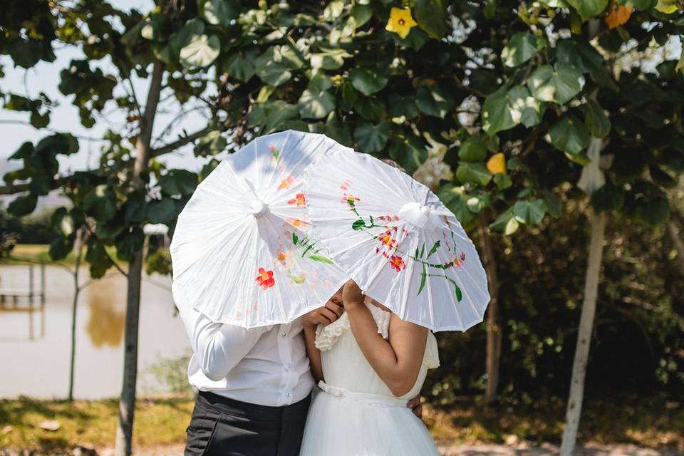 Novios en el jardín tapando su caras con sombrillas