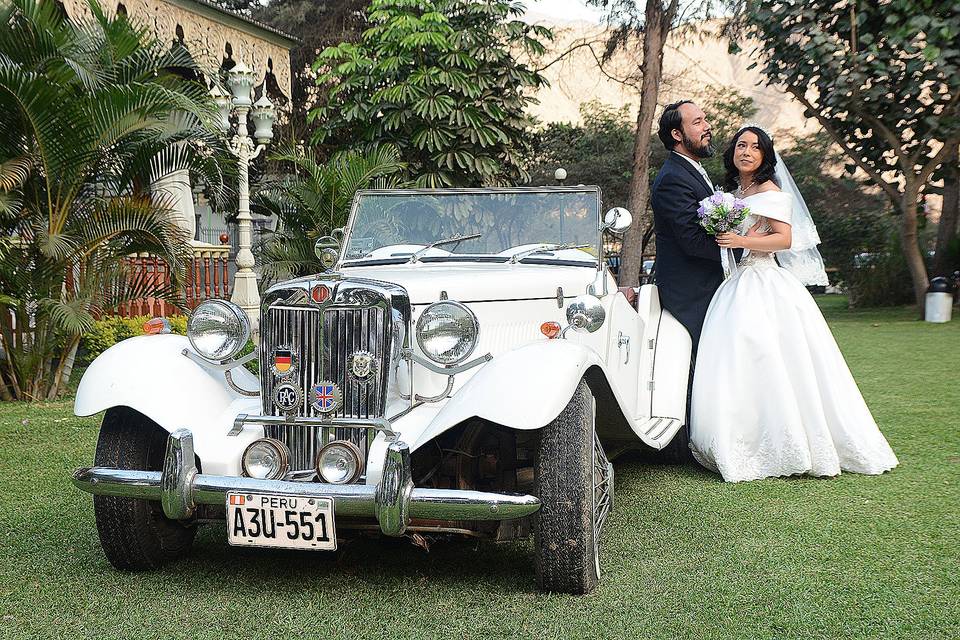 Novios posando con un auto clásico blanco