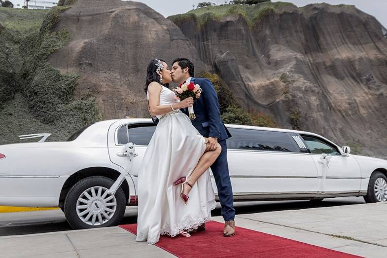 Novios dándose un beso frente al auto blanco