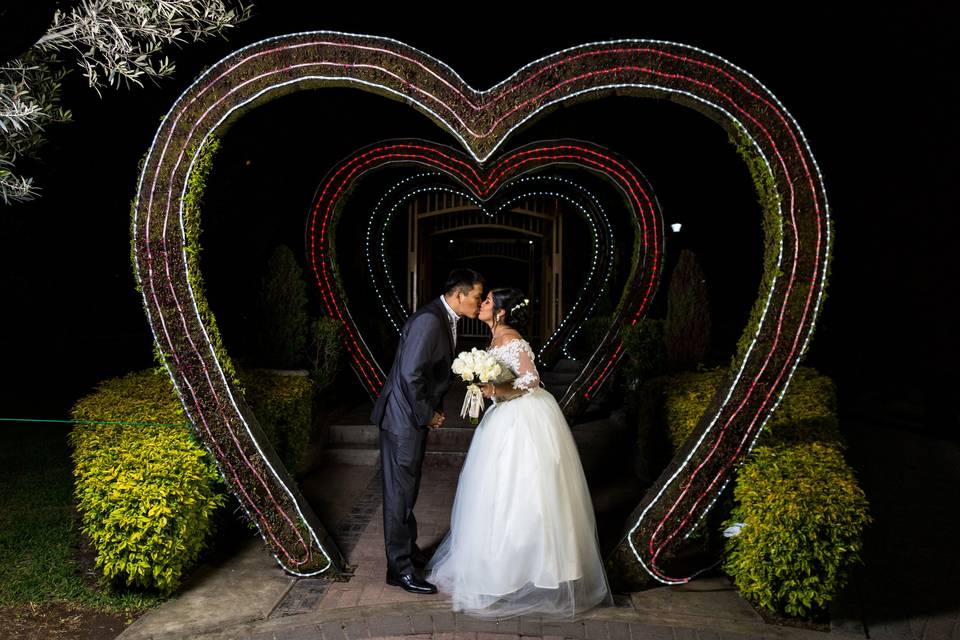 Novios dándose un beso bajo un corazón de flores