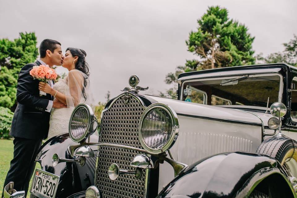 Novios besándose frente a un auto clásico