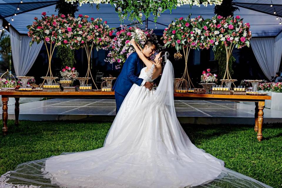 Novios posando frente a una mesa de postres decorada con muchas flores